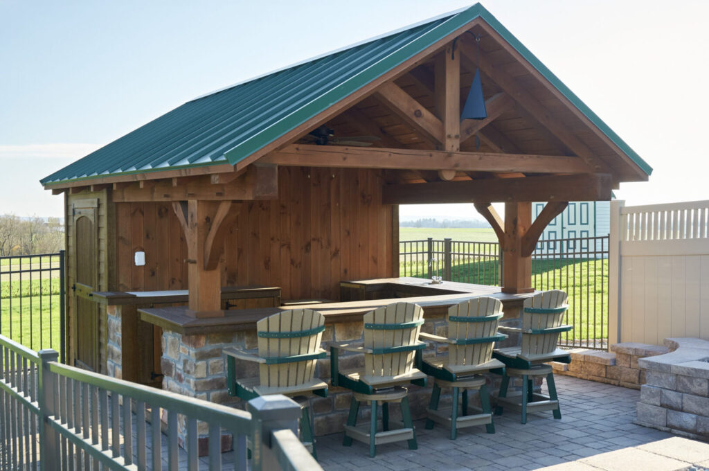 A small outdoor kitchen featuring a bar with chairs, set in a sunny garden environment.