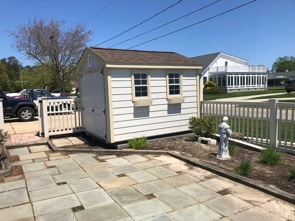 A small white shed surrounded by a wooden fence in a grassy area.