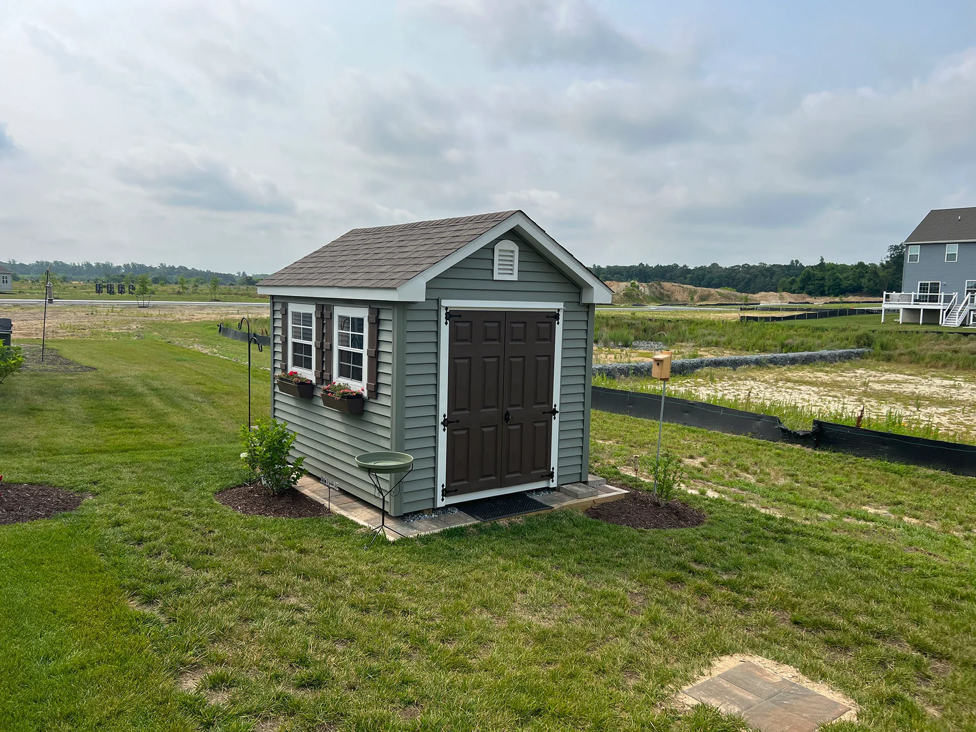 A small shed stands alone in the center of a vast green field under a clear blue sky.