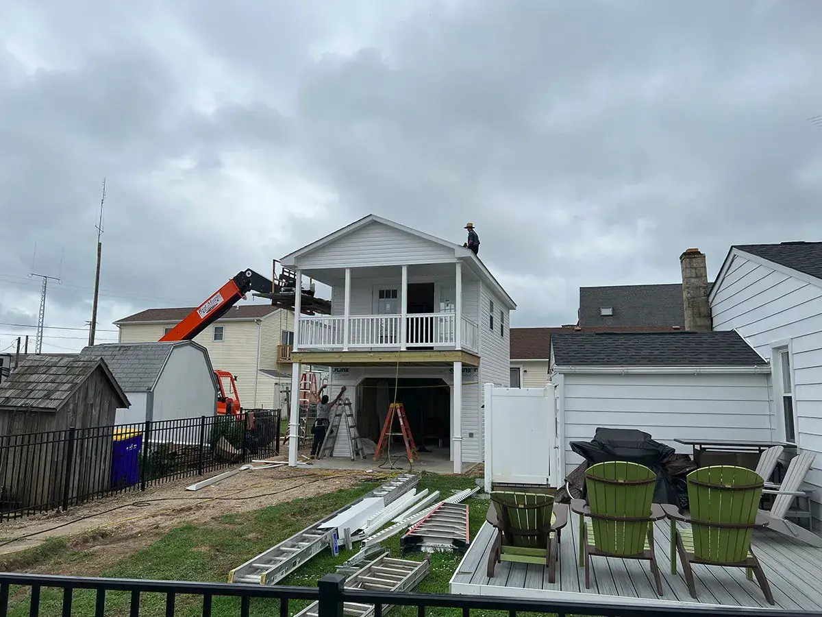 A man stands on a ladder, installing a roof on a house under clear blue skies.
