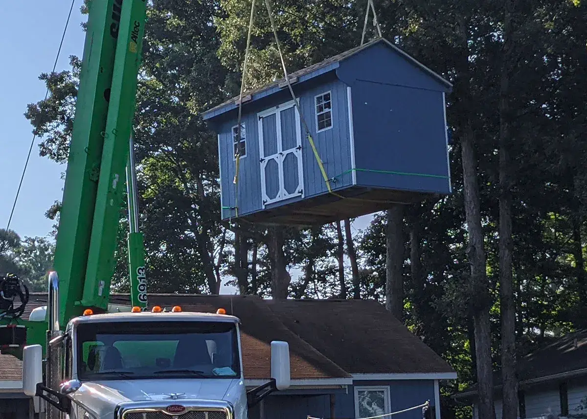 A truck is lifting a blue house off its bed, showcasing the house's structure and the truck's lifting mechanism.