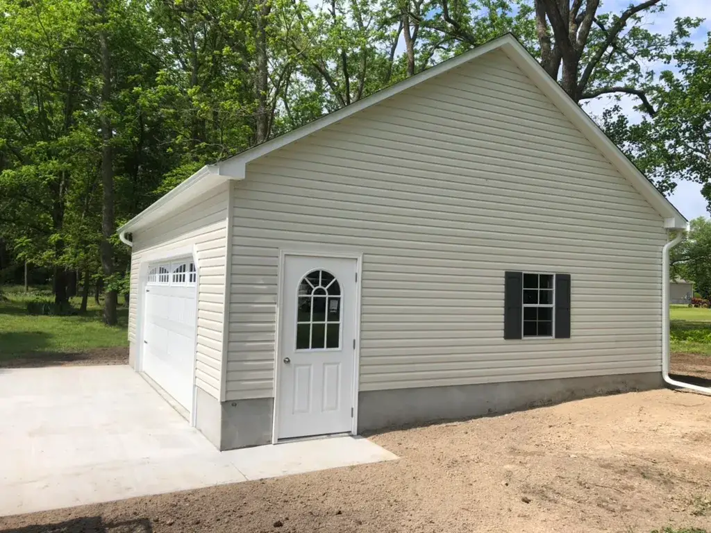 A garage featuring white siding and a closed door, set against a clear sky.