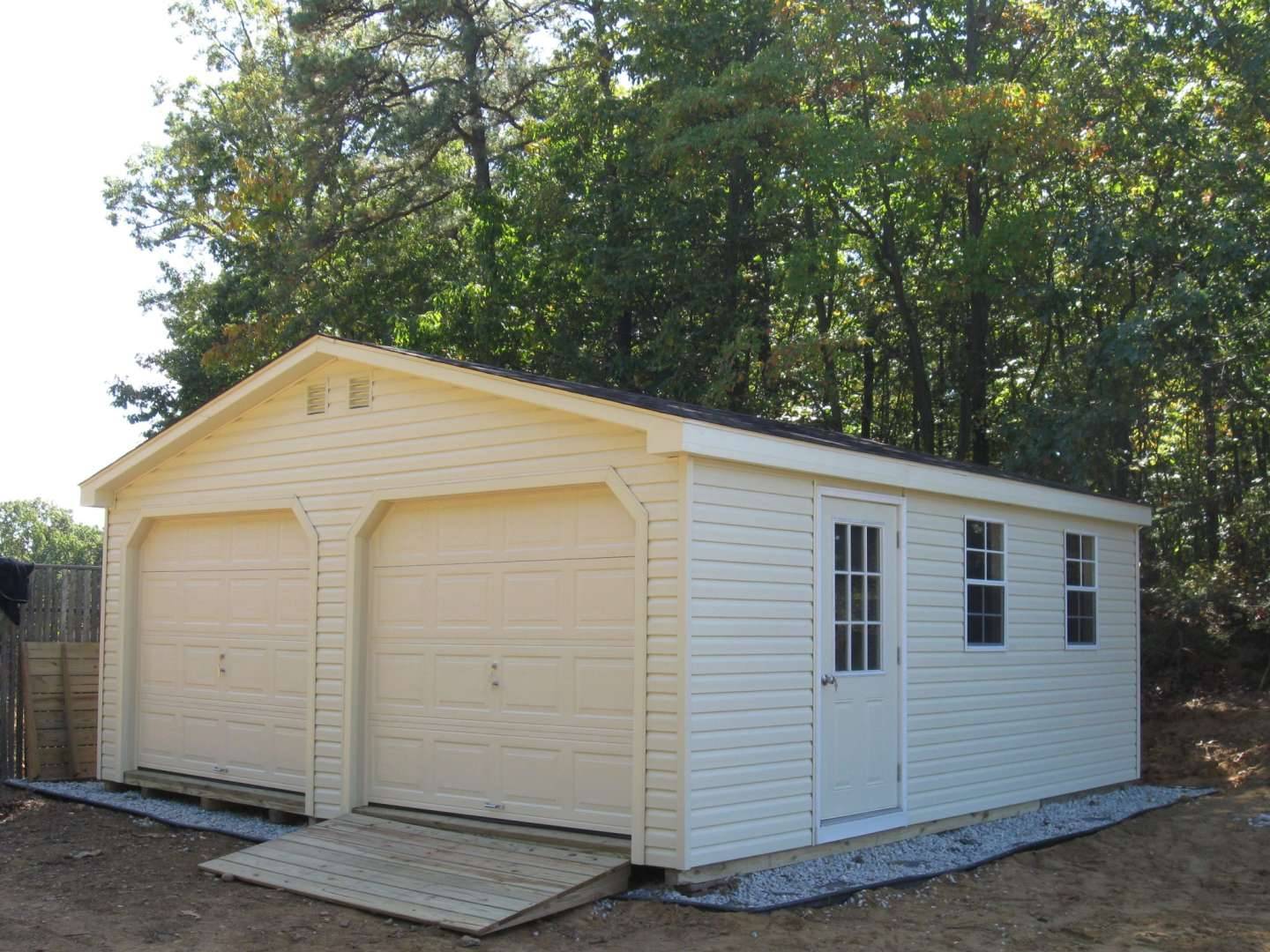 A compact white garage with two doors, surrounded by greenery.