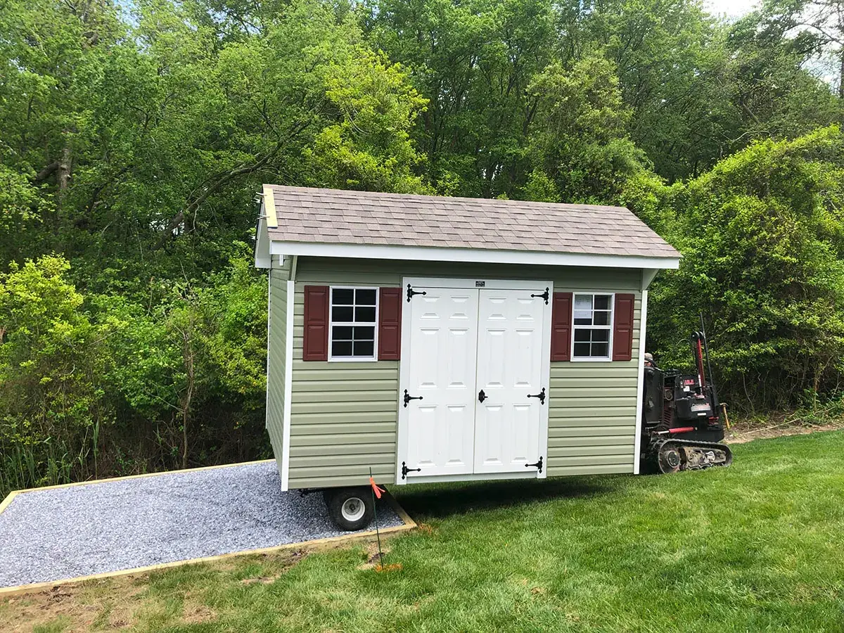 A small shed on a trailer positioned in a grassy yard, surrounded by trees and open space.